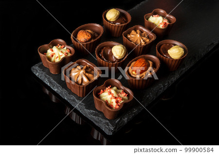 Candy with cream and nuts on a slate board. Assorted chocolate on black isolated background. Idea for dessert in restaurant 99900584