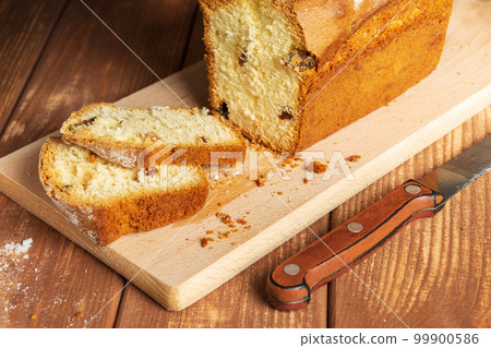 Sliced homemade cupcake with raisins sprinkled with powdered sugar on a wooden cutting board and knife Sliced homemade cupcake with raisins sprinkled with powdered sugar on a wooden cutting board and knife 99900586