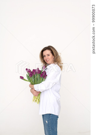 Cute girl in a white shirt hugging a large bouquet of purple tulips on a white background Cute girl in a white shirt hugging a large bouquet of purple tulips on a white background 99900873