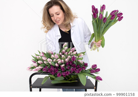 Cute florist girl in a shirt collects a bouquet of purple and white tulips for a birthday present Cute florist girl in a shirt collects a bouquet of purple and white tulips for a birthday present 99901158
