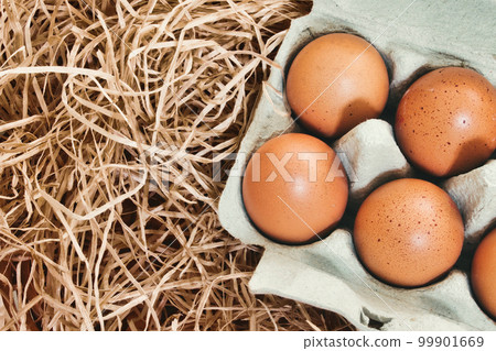 Close-up of brown chicken's eggs in a cardboard carton against straw background 99901669