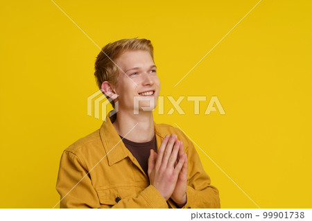 Happiness Gratitude Faith Concept. Smiling Young European Man Joined His Palms in a Gesture of Gratitude on a Yellow Background. High quality photo Happiness Gratitude Faith Concept. Smiling Young European Man Joined His Palms in a Gesture of Gratitude on a Yellow Background. High quality photo 99901738