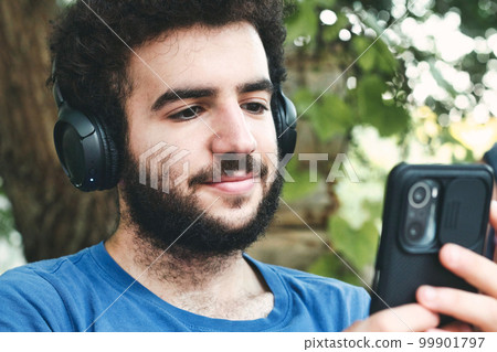 Close-up headshot of a young man wearing a blue t-shirt listening to modern music on his mobile phone with big wireless headphones 99901797