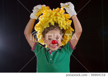 Little boy clown. Child in a clown wig with a red nose close up Little boy clown. Child in a clown wig with a red nose close up 99904158