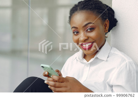 Black girl in the office. Woman in a white shirt. Lady use the phone. 99906762