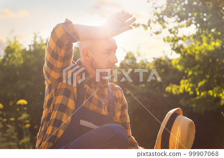 Summer heat. Portrait of a bearded adult gardener wiping sweat from his forehead. Gardening and Horticulture Concept Summer heat. Portrait of a bearded adult gardener wiping sweat from his forehead. Gardening and Horticulture Concept 99907068