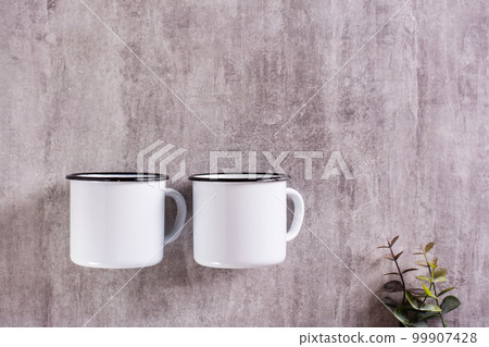 Two white empty metal mugs on a gray background with a place for an inscription. Top view 99907428