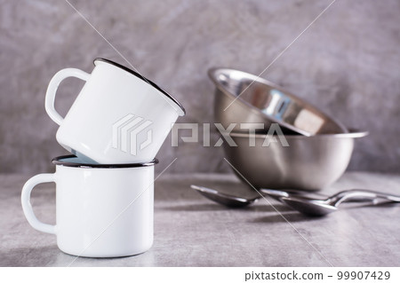 Two white empty metal mugs and metal bowls and spoons on a gray background 99907429