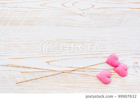 Three pink knitted hearts on sticks on a white wooden background. Copy space 99907632