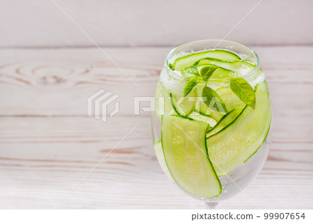 Refreshing water with slices of cucumber and basil leaves in a glass Refreshing water with slices of cucumber and basil leaves in a glass 99907654