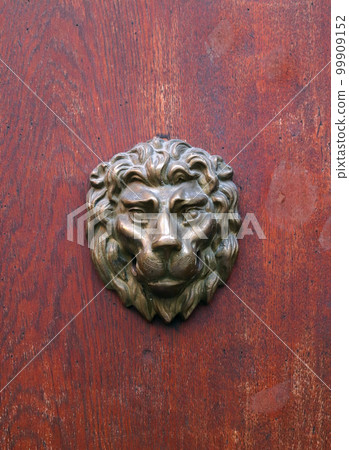 Bronze head of lion on red wooden texture. Head of lion on red door. 99909152