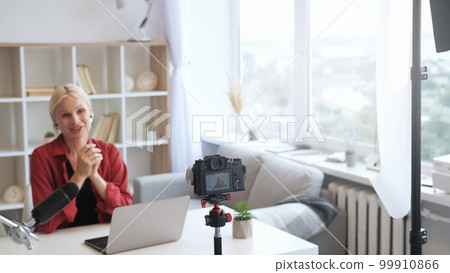 Home vlog. Blogger broadcast. Influencer lifestyle. Mature expert woman talking recording video content on camera on tripod at defocused modern studio window with free space. 99910866