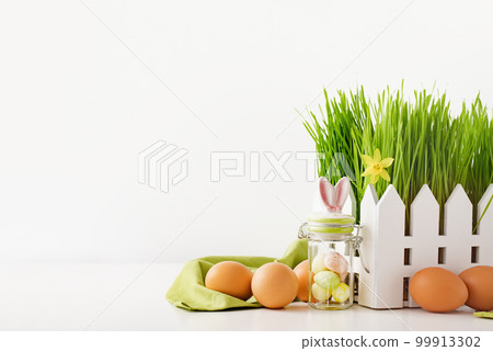 Happy Easter concept. Green grass meadow with fence and bunny ears jar. Several natural brown eggs in front of it. Easter holiday eggs hunt and painting concept. 99913302