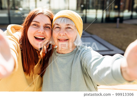 Two women together wear casual clothes doing selfie shot pov on mobile cell phone. Family day concept. Young woman and senior middle aged mom spending time together 99913306