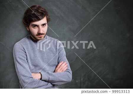 A portrait of serious young bearded guy with stylish hairstyle dressed in casual sweater standing crossed hands looking serious and confident. A portrait of serious young bearded guy with stylish hairstyle dressed in casual sweater standing crossed hands looking serious and confident. 99913313