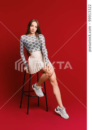 Cute sporty young woman sitting on a tall chair against ruby red background 99913322