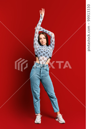 Young woman posing on red wall background with lifted arm Young woman posing on red wall background with lifted arm 99913330