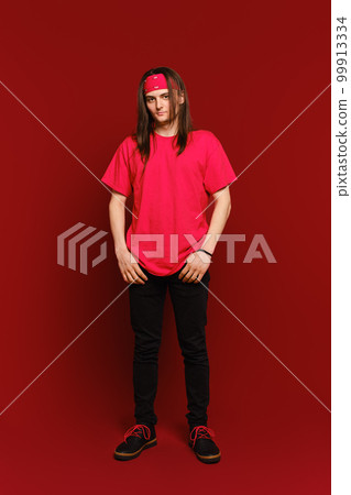 Indoor portrait of positive good-looking hipster guy wearing red band on head, standing against red wall 99913334