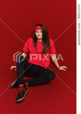 Man with long hair sitting on floor in red studio 99913341
