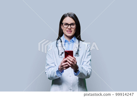 Young woman doctor using smartphone on light gray background Young woman doctor using smartphone on light gray background 99914247