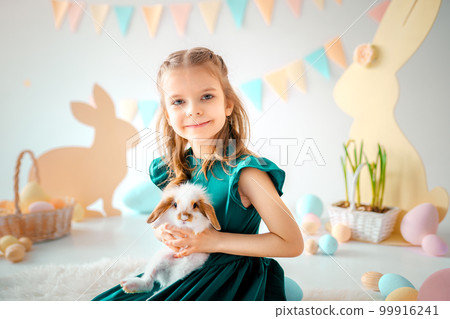 Happy little girl holds fluffy rabbit on Easter colorful decor background. Easter concept  99916241