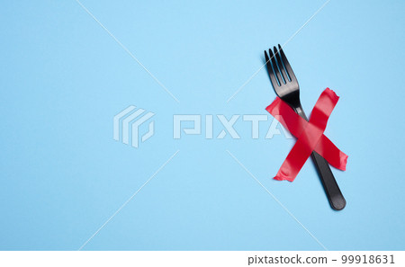 A plastic fork is attached with red adhesive tape on a blue background, a concept of refusing plastic tableware and recycling materials, zero waste A plastic fork is attached with red adhesive tape on a blue background, a concept of refusing plastic tableware and recycling materials, zero waste 99918631