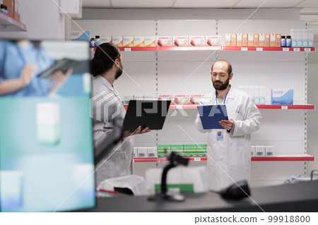 Drugstore workers working at pharmaceutical pills inventory checking drugs packages writing medical info on papers. Pharmacy is a vital resource for patients in need of medication and treatment. Drugstore workers working at pharmaceutical pills inventory checking drugs packages writing medical info on papers. Pharmacy is a vital resource for patients in need of medication and treatment. 99918800