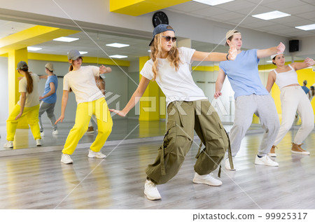 Diligent teenagers leaning back on their toes during modern dance rehearsal in spacious hall 99925317