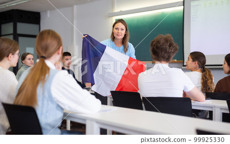 Geography lesson in school class - teacher talks about France, holding flag in his hands Geography lesson in school class - teacher talks about France, holding flag in his hands 99925330