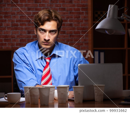 Young employee drinking coffee working at night shift Young employee drinking coffee working at night shift 99931662