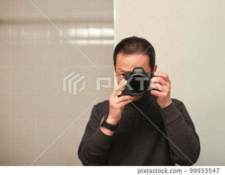 A male photographer taking a selfie looking at the mirror indoors 99933547