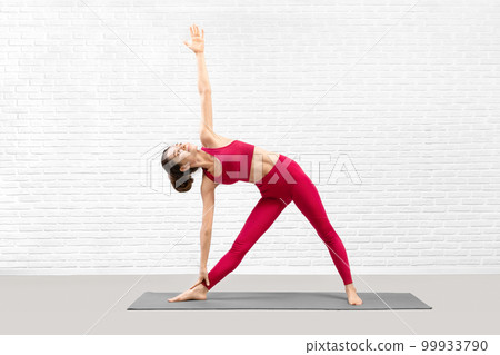 Attractive young woman does triangle pose in fitness studio indoor, Trikonasana. Attractive young woman does triangle pose in fitness studio indoor, Trikonasana. 99933790