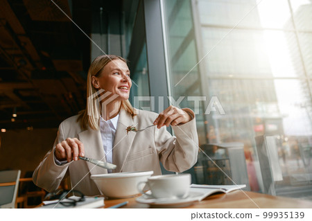 Cheerful businesswoman is having a business lunch during working day in cafe. Blurred background 99935139