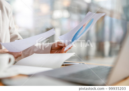 Close up of businesswoman working with documents and use laptop while sitting in cafe near window 99935203
