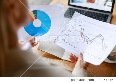 Close up of businesswoman making videoconference and demonstrate financial graphs to colleague Close up of businesswoman making videoconference and demonstrate financial graphs to colleague 99935256