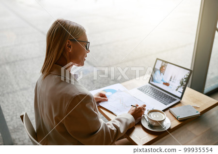 Businesswoman making online videoconference and discuss project with colleague in cafe near window Businesswoman making online videoconference and discuss project with colleague in cafe near window 99935554