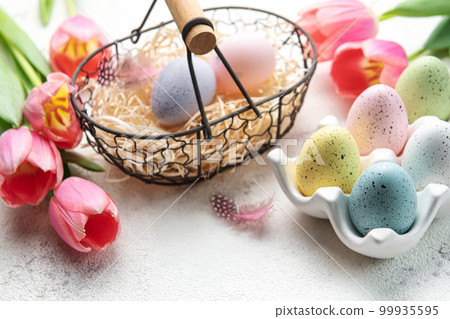 Basket with Easter eggs painted  pastel colors and pink tulips on a concrete background. 99935595
