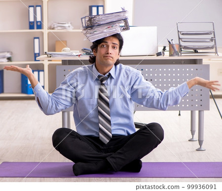 Young handsome male employee doing exercises in the office 99936091