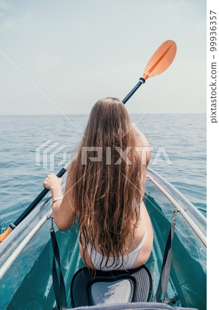 Woman in kayak back view. Happy young woman with long hair floating in transparent kayak on the crystal clear sea. Summer holiday vacation and cheerful female people relaxing having fun on the boat 99936357