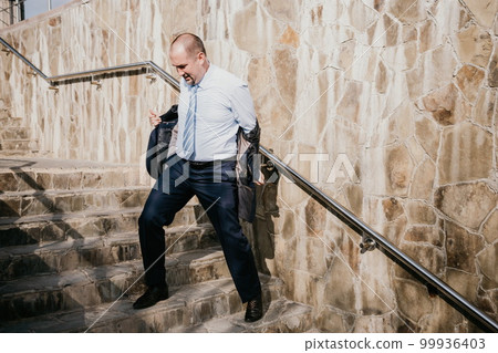 Portrait of a senior professional man in a suit with various problems. A middle-aged businessman with descends the stairs. 99936403