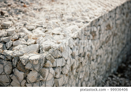 Granite stones behind a metal grate for strengthening the slope. Stones behind the wire. grey texture. construction. Granite stones behind a metal grate for strengthening the slope. Stones behind the wire. grey texture. construction. 99936406