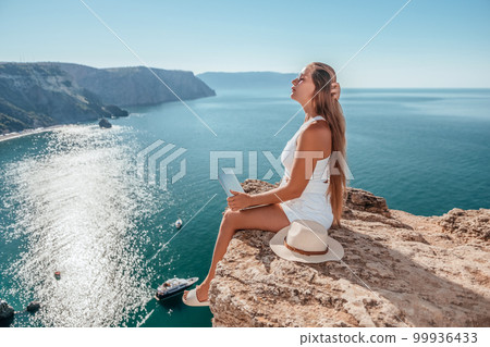 Digital nomad, Business woman working on laptop by the sea. Pretty lady typing on computer by the sea at sunset, makes a business transaction online from a distance. Freelance, remote work on vacation 99936433
