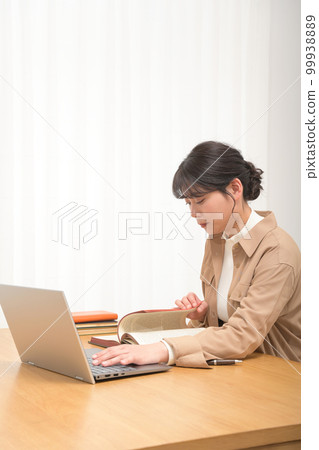 一位年輕女性在閱讀一本舊英文書時在筆記本電腦上進行研究 一位年輕女性在閱讀一本舊英文書時在筆記本電腦上進行研究 99938889