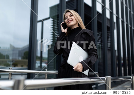 confident female european leader speaks on the phone on the background of the business center 99940525