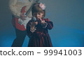 Little girl on stage in vintage dress, she sings into microphone and dances, her father plays an electric guitar. Color music is shining and smoke is billowing. Family time, creativity and hobbies 99941003
