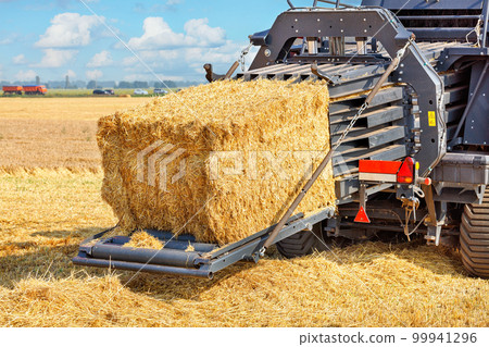 A fragment of an agricultural tractor forming bales of straw against the background of a field. A fragment of an agricultural tractor forming bales of straw against the background of a field. 99941296