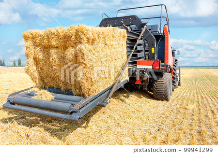 A modern agricultural machine collects straw into large bales after the end of the wheat harvest. A modern agricultural machine collects straw into large bales after the end of the wheat harvest. 99941299