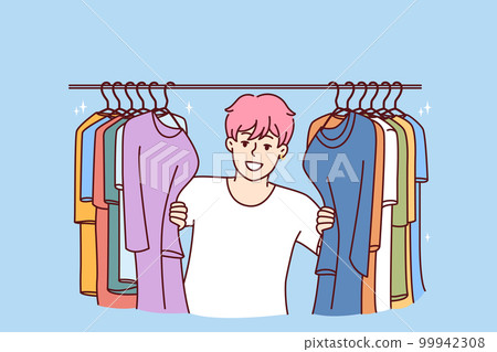 Young Cheerful man in t-shirt smiling peeking out from behind hanger for collection of clothes 99942308