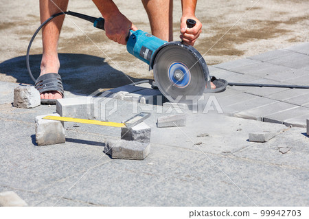 A worker cuts paving slabs with a grinder with a diamond blade. Selective focus, copy space. A worker cuts paving slabs with a grinder with a diamond blade. Selective focus, copy space. 99942703