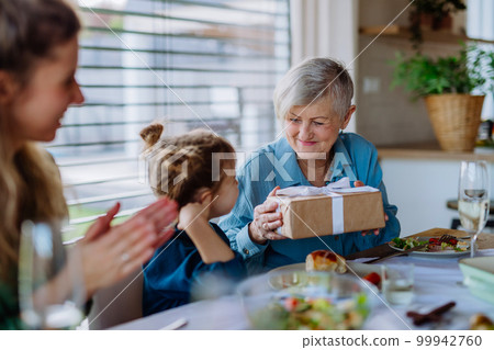 Grandmother giving gift to her granddaughter during Easter dinner. 99942760